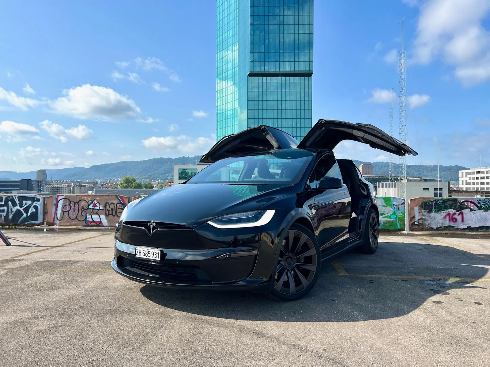 Tesla Model X Plaid nera con portiere ad ali di gabbiano aperte davanti alla Prime Tower a Zurigo